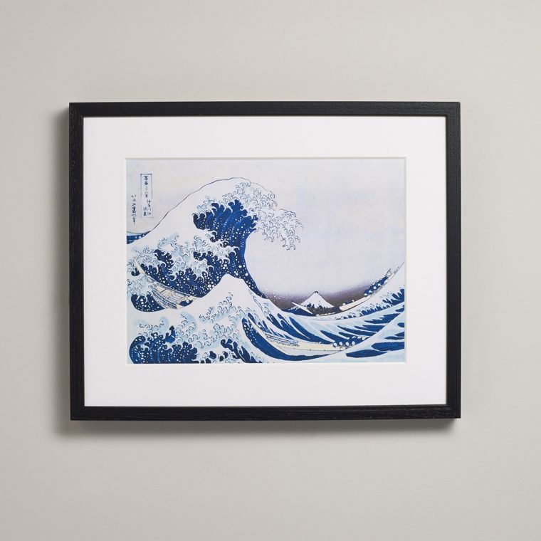 A landscape print in a black box frame with a wide white mount, hung on a pale wall